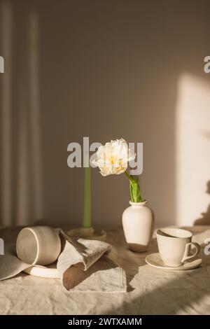 Nahaufnahme einer gelben Tulpe in einer Vase auf einem Tisch mit verschiedenen Keramiken im Sonnenlicht Stockfoto