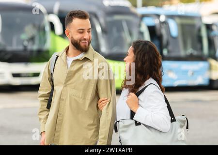 Lächelndes junges Paar, das mit Taschen an der Bushaltestelle spaziert und plaudert Stockfoto