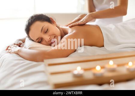 Friedliche Frau bei Massagesitzung liegend und genießt Schönheitsbehandlungen im Haus Stockfoto