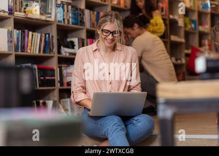 Porträt einer jungen Studentin, die mit ihren Freunden im Hintergrund in der Bibliothek sitzt. Stockfoto