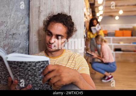 Porträt eines jungen männlichen Studenten, der in der Bibliothek sitzt und ein Buch liest. Stockfoto