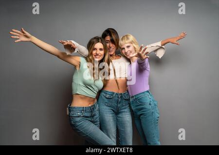Drei fröhliche junge Frauen teilen einen fröhlichen Moment - verspielte Posen, trendige Freizeitmode, echte Glücksausdrücke, verbindende Zeit, energiegeladenes A Stockfoto