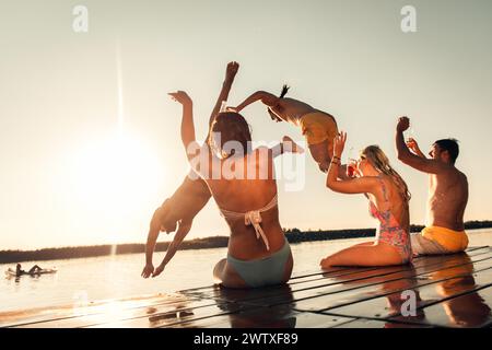 Freunde, die Spaß am Sommertag haben, schwimmen und springen auf dem See. Stockfoto