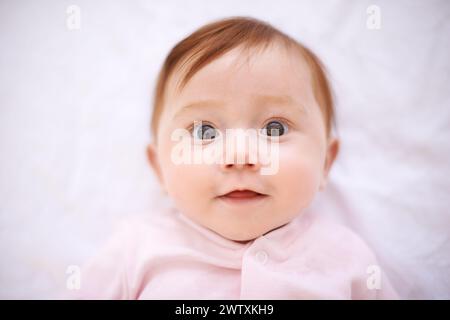 Glücklich, Baby und Porträt eines Mädchens im Bett mit Lächeln für Kindheit, Entwicklung und Entspannung im Kinderzimmer. Neugeborene, Ruhe und Gesicht des Kindes mit Frieden für Stockfoto