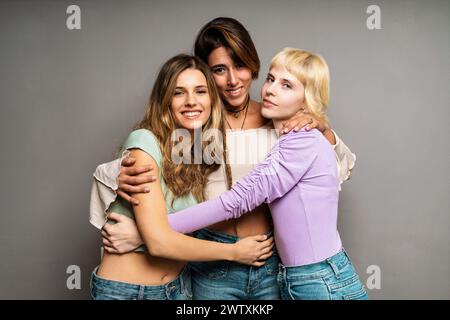 Gruppe von drei jungen Frauen - umarmen - multirassische Freundinnen, die lächeln, sich verbinden und umarmen - Vielfalt und Zusammengehörigkeit vertreten; Stockfoto