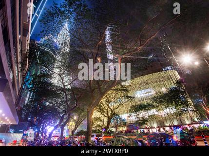 Wolken beleuchtet durch helle Lichter von hohen Gebäuden, geschäftiges Stadtleben, umrahmt von Bäumen, Ampeln und Lichtstreifen von vorbeifahrenden Traff Stockfoto