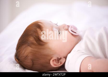 Baby, Schnuller und entspannen Sie sich auf dem Bett zu Hause für Wellness, Ruhe und Erholung am Morgen im Kinderzimmer. Säugling, Neugeborenes und Frieden mit Schnuller, Wachstum und Stockfoto