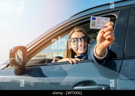 Glückliche Frau, die ihren neuen Führerschein am sonnigen Tag aus dem Fenster zeigt Stockfoto