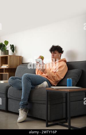 Männlicher Schüler mit Apfel und Tablet-Computer, der zu Hause auf dem Sofa sitzt Stockfoto