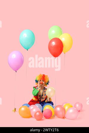 Lustiger kleiner Junge im Clown-Kostüm mit Ballons auf rosa Hintergrund. Feierlichkeiten zum Aprilfeiertag Stockfoto