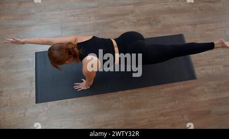 Schönes, sportliches Mädchen, das zu Hause Yoga oder Pilates übt. Medien. Draufsicht einer Frau, die Gleichgewichtsübungen macht und Arm und Bein dehnt. Stockfoto