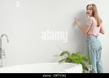 Eine unzufriedene junge Frau, die auf Schimmel an der Wand im Badezimmer zeigt Stockfoto