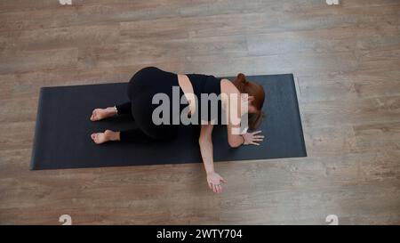 Frau in schwarzer Activewear, die Yoga Asanas auf Matte im Yoga-Kurs macht. Medien. Gesunder Lebensstil, Trainingskonzept. Stockfoto