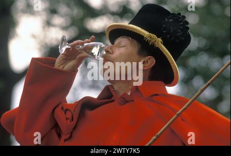 Königlicher Kutscher mit Hut und rotem Mantel, er hat einen Gast vom Buckingham Palace zu einem Empfang gebracht. Er trinkt Champagner. London, England um 1995. HOMER SYKES AUS DEN 1990ER JAHREN Stockfoto