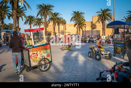 Ein junges Mädchen fährt mit einem Spielzeugroller an einem dekorierten Pferd auf dem Bourguiba-Platz, neben dem Ribat, Monastir, Tunesien Stockfoto