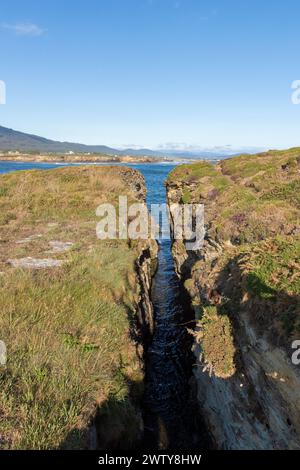 Ruhige natürliche Landschaft mit einem schmalen Wasserkanal, der zu einem größeren Gewässer unter klarem Himmel führt Stockfoto