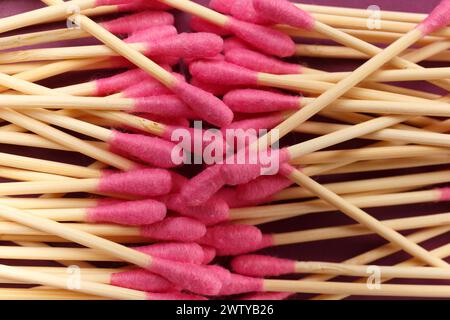 Rosafarbene Bambus-Wattestäbchen sind auf einem violetten Hintergrund verstreut, Draufsicht, Nahaufnahme. Umweltfreundliche Artikel für Hygiene, Make-up, Medizin. Stockfoto