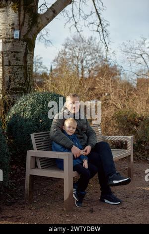 Herbstliche Familienzusammenhänge: Vater, 40 Jahre alt, und Sohn - wunderschöner 8-jähriger Junge, im Park sitzend. Stockfoto