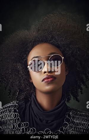 Porträt einer jungen afroamerikanischen Frau mit lockigem Haar, Sonnenbrille und Kettenpost, stehend vor Vintage-grünem Hintergrund. Stockfoto