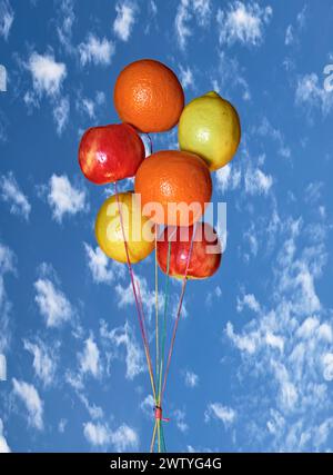 Äpfel, Orangen und Zitronen, die wie Ballons aussehen. Auf einem hellen, himmelblauen Hintergrund. Stockfoto