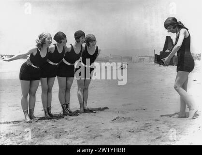 Vier von Mack Sennetts „Badeschönheiten“ in einteiligen Kostümen werden von einem Fünftel am Strand fotografiert Stockfoto