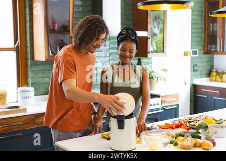 Ein vielseitiges Paar legt Essensabfälle in den Kompostbehälter zusammen in der Küche Stockfoto