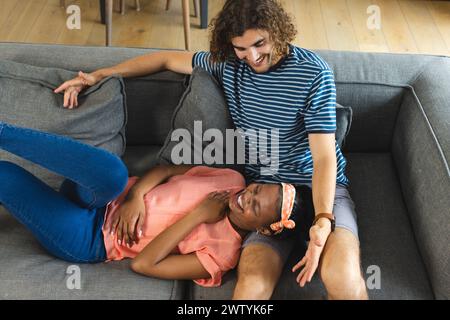 Ein vielseitiges Paar teilt sich einen verspielten Moment auf einer grauen Couch zu Hause Stockfoto