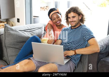 Ein vielseitiges Paar entspannt sich auf dem Sofa mit einem Laptop zu Hause Stockfoto