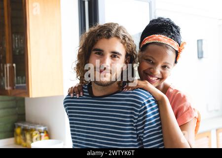 Ein vielseitiges Paar teilt sich zu Hause eine warme Umarmung und lächelt zufrieden Stockfoto