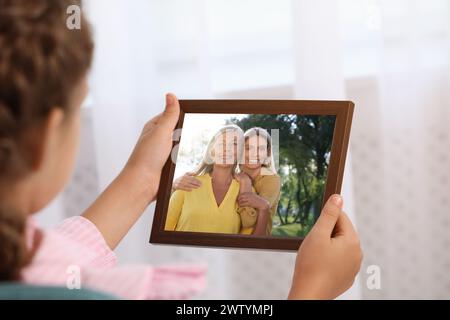 Kleines Mädchen mit Rahmen mit Foto-Porträt ihrer Familie drinnen, Nahaufnahme Stockfoto