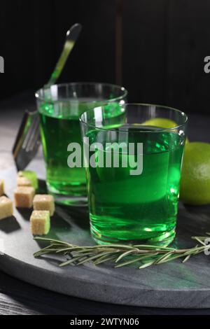 Absinth in Gläsern, Rosmarin, brauner Zucker und Limette auf dem Tisch. Alkoholisches Getränk Stockfoto