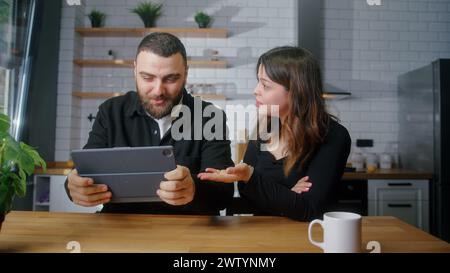 Junge Liebhaber sitzen in der Küche, Mann spielt ein Rennspiel auf Tablet-Computer, Frau, die sich mit ihrem Freund anlegt Stockfoto