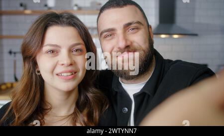 Nahaufnahme junger glücklicher Paare sitzen in der Küche und unterhalten sich mit Freunden oder Familie über Videoanrufe. Videoanrufe im Online-Chat über das Smartphone unter Stockfoto