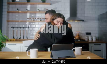 Junge Paare sitzen in der Küche Tablet lesen Sie tolle Nachrichten online erhalten E-Mail Freude feiern Gelegenheit sich gegenseitig umarmen Stockfoto