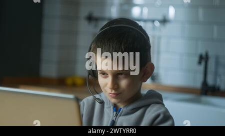 Nahaufnahme eines Schülers, der ein schnurloses Headset trägt, während eines Videogesprächs mit einem Laptop online kommuniziert und dem Lehrer zuhause zuhört. Online-Pfleger Stockfoto