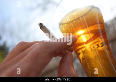 ILLUSTRATION - 20. März 2024, Bayern, Kaufbeuren: Eine Hand hält einen Joint neben einem Glas Bier. Der Bundestag verabschiedete die kontrollierte Freilassung am 1. April. Die Entscheidung des Bundesrates steht jedoch noch aus. Für die umstrittene Legalisierung von Cannabis am kommenden Freitag, den 22. März, gibt es im Bundesrat noch keine klare Mehrheit. Foto: Karl-Josef Hildenbrand/dpa Stockfoto