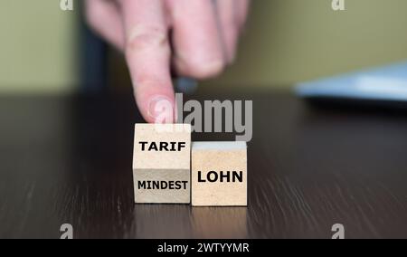 Die Hand dreht Holzwürfel und ändert das deutsche Wort "Mindestlohn" in "Tariflohn". Stockfoto