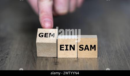 Hand dreht Holzwürfel und ändert das deutsche Wort „einsam“ in „gemeinsam“. Stockfoto