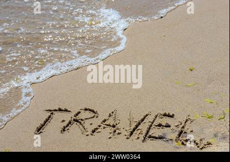 Reisekonzept - Beschriftung im Sand. Sandige Küste des Meeres. Motivation. Meereswelle. Das Wort Reisen steht am Strand. Urlaub am Th Stockfoto