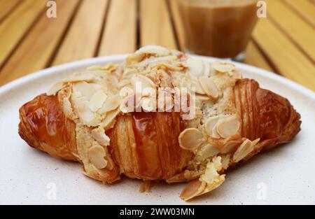 Köstliches Mandelcroissant mit einer Tasse Kaffee im Hintergrund Stockfoto