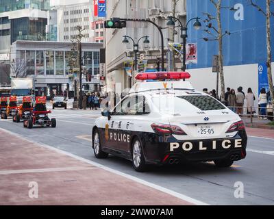 TOKIO, JAPAN - 19. März 2024: Ein Polizeiauto, das hinter einer Linie von Miet-Go-Carts auf einer Straße in der Nähe des Bahnhofs Shibuya in Tokio fährt. Stockfoto