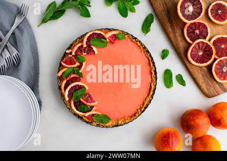 Blood Orange Cheesecake Tart auf einem weißen Marmortisch: Himbeerorange Quark Käsekuchen Tarte garniert mit Minzblättern in graham Cracker Kruste Stockfoto