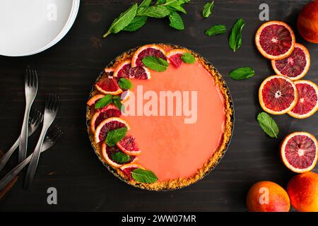 Blood Orange Cheesecake Tart auf einem rustikalen Holztisch: Himbeerorange Quark Käsekuchen Tarte garniert mit Minzblättern in graham Cracker Kruste Stockfoto