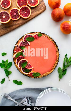 Blood Orange Cheesecake Tart auf einem weißen Marmortisch: Himbeerorange Quark Käsekuchen Tarte garniert mit Minzblättern in graham Cracker Kruste Stockfoto