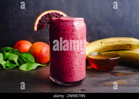 Blood Orange Mixed Berry Smoothie mit Zutaten: Frisch zubereitetes Frühstück Smoothie mit Blutorangen und Baby-Spincah-Blättern im Hintergrund Stockfoto