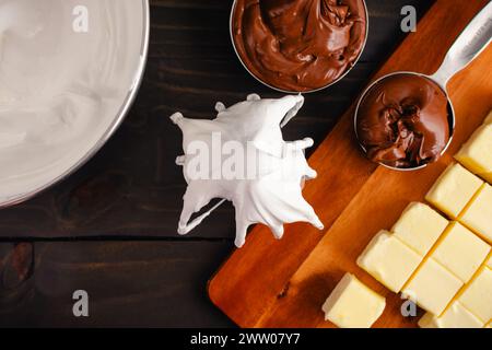 Mit Meringue überzogener Quirlenaufsatz für den Standmixer: Der Quirlenaufsatz wird in eine Schüssel mit Schweizer Quirle in der Nähe von zerrissenen Eiern und Butter gelegt Stockfoto