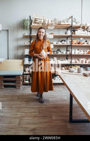 Keramikkünstlerin hält eine handwerkliche Tonvase im Sunny Studio Stockfoto