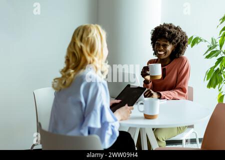 Zwei Frauen teilen sich einen freudigen Moment, plaudern und trinken Kaffee in einem lichtdurchfluteten Café Stockfoto