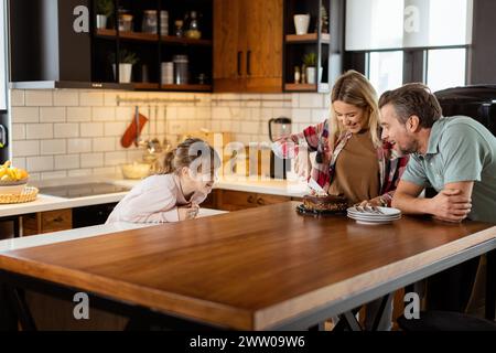 Eine herzerwärmende Szene entfaltet sich, während eine Familie einen köstlichen Schokoladenkuchen zusammen in der Wärme ihrer sonnendurchfluteten Küche genießt und Lächeln und cr teilt Stockfoto