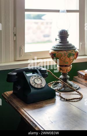 Altes schwarzes Telefon neben dem Fenster mit einer alten Kerosin-Lampe auf einem Holztisch. Stockfoto